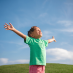 a child with arms outstretched in a grassy field