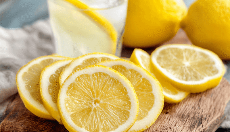 레몬 효능 5가지와 건강한 레몬수 만드는 법 yellow lemon slices arranged on a rustic wooden cutting board, with a refreshing glass of lemonade beside it