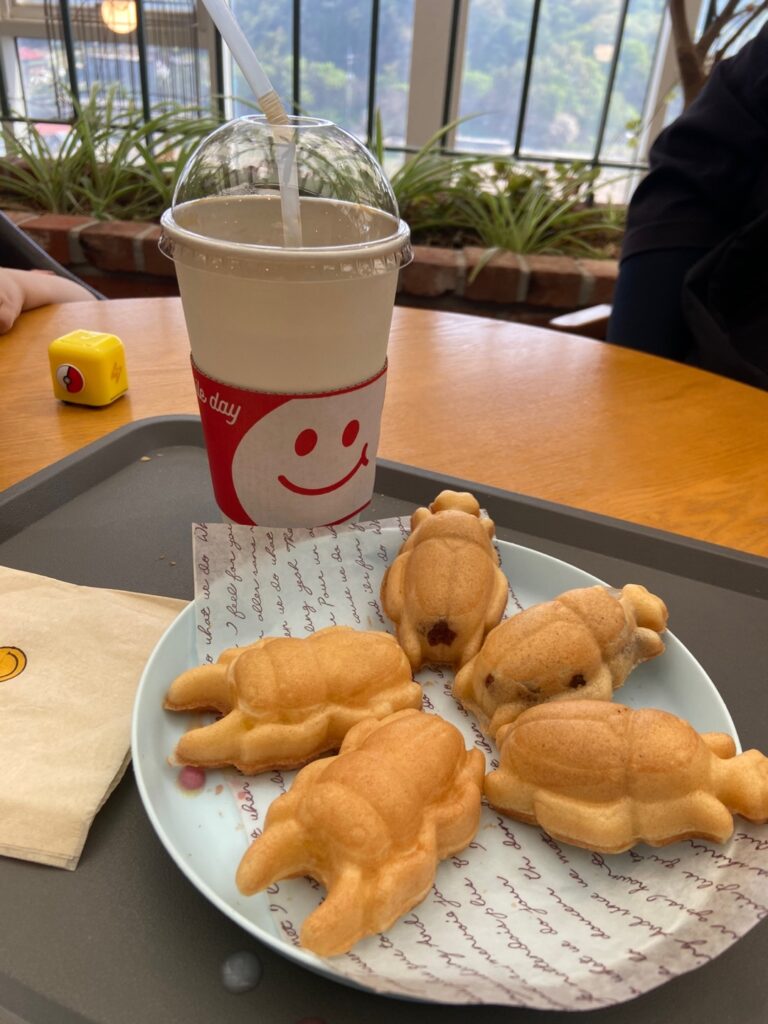 Plate of several animal-shaped pastries on a light blue plate, with a large soda in a red-smiley cup on a gray tray in a cafe setting.
