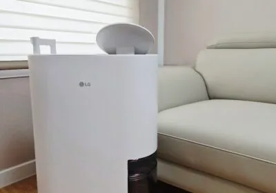 거실 소파 옆에 놓인 흰색 LG 휘센 오브제컬렉션 제습기 DQ134MWEC, 하단에 투명 물통이 보이는 모습