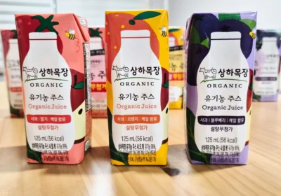 상하목장 유기농 주스 3종 - Useful Life Hub 나무 테이블 위에 나란히 놓인 상하목장 유기농 주스 3종 팩 — 왼쪽부터 사과딸기케일, 사과오렌지케일, 사과블루베리케일, 각 125mL 설탕무첨가 표기