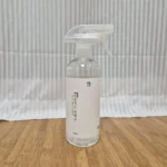 살림백서 피톤치드 편백수 500ml 트리거 스프레이 병이 원목 마루 위에 세워져 있는 사진 — 투명 용기에 담긴 맑은 편백수와 세로쓰기 라벨, "매일 아침 편백향으로 상쾌하게" 문구가 보인다.