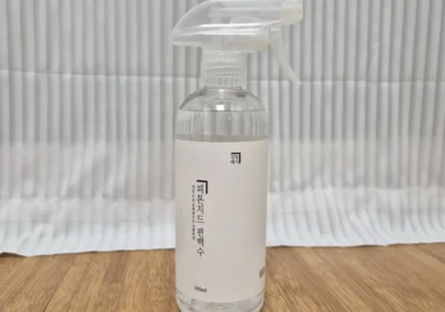 살림백서 피톤치드 편백수 500ml 트리거 스프레이 병이 원목 마루 위에 세워져 있는 사진 — 투명 용기에 담긴 맑은 편백수와 세로쓰기 라벨, "매일 아침 편백향으로 상쾌하게" 문구가 보인다.