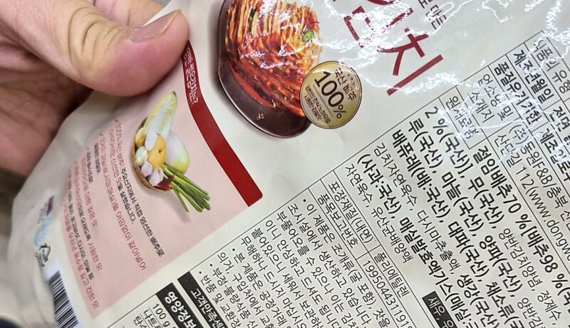 마트 포장김치 뒷면 원산지 표시 직접 확인 - Useful Life Hub 마트에서 동원F&B 양반 썰은김치 봉지를 손으로 뒤집어 뒷면 원재료명과 원산지 표시란을 확인하는 모습